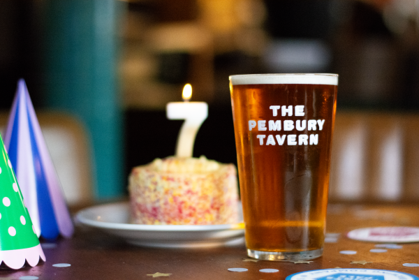Pint of beer in front of a birthday cake with a candle with the number 7 on it.