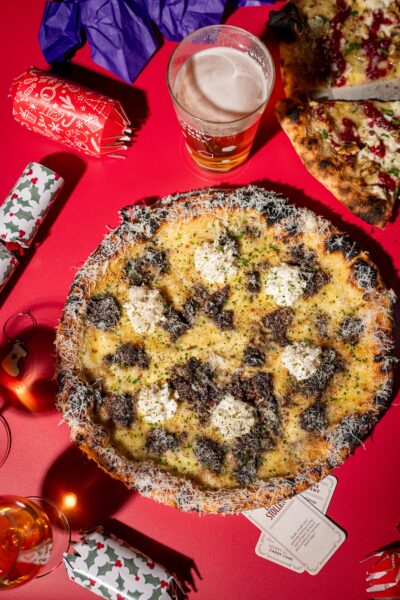 The beefy Christmas Pizza Special, A Tuscan Christmas, is shown amid some Christmas props and a beer
