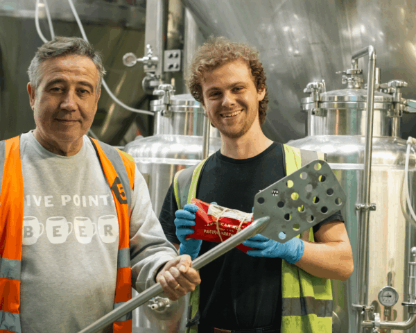 Bradley and Noah from Five Points pose, with Bradley holding a mash paddle and Noah holding a small bag of hops.
